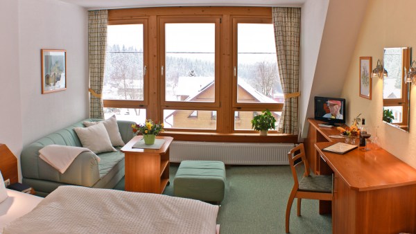 Hotelzimmer mit Bett, Sofa, Tisch, Fernseher, 3-Teile Fenster. Sauber und dekoriert.