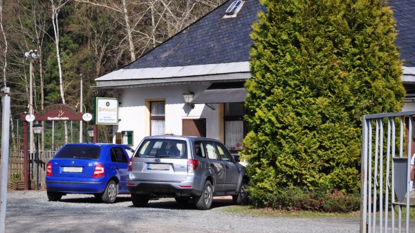 Zwei Autos parken vorm Sportlerheim. Daneben ist der Eingang zum Biergarten.