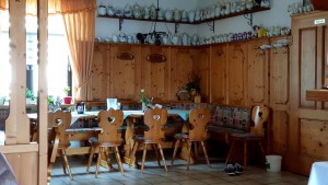 Sitzecke aus Holz mit gedecktem Tisch im Gastraum. Oben stehen viele Kaffeekannen.