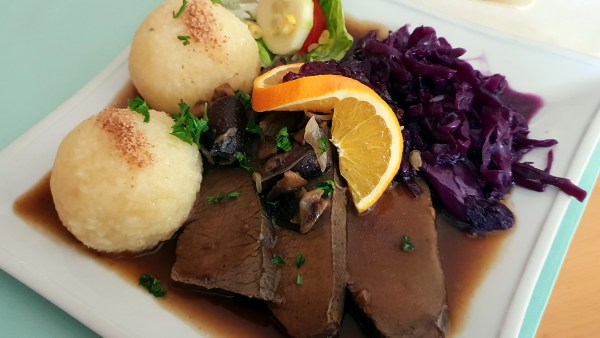 Fleisch mit Klöße und Rotkohl, garniert mit Apfelsinen-Scheibe und Soße und Salat