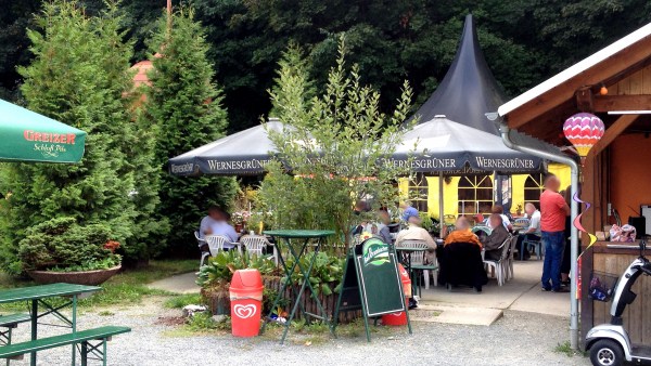 Stehtisch neben Papierkorb mit Gästen im biergarten unter Sonnenschirmen