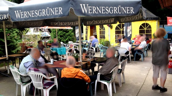 Besucher sitzen auf Gartenstühle unter Sonnenschirm