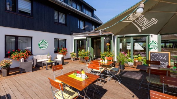 Gartenmöbel auf Holzterrasse. Restaurant-Tische sind gedeckt. Terrasse vor Haus und Nebengang teilweise überschirmt mit Wernesgrüner-Schirm