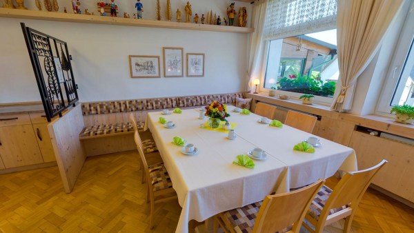 Gedeckter Tisch am Fenster in Gaststube mit Trennwand. Viele Holzfiguren auf Regal oben.