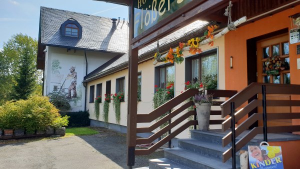 Haus mit Wandmalerei, Blumen in Fenstern, Treppe und Geländer zur Eingangstür