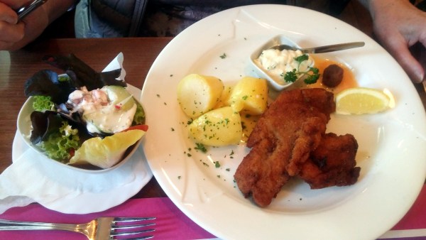 Schnitzel mit Kartoffeln auf Teller, daneben eine Schüssel mit Salat