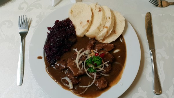 Wildgericht auf Teller mit Besteck: Hirschgulasch mit böhmischen Klössen und Rotkraut