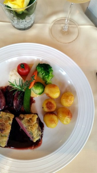 Teller mit Tomate, Brokkoli, Rosenkohl, Mohre, Erbsen, Kartoffeln, Fleisch, Soße auf Teller auf gedecktem Tisch