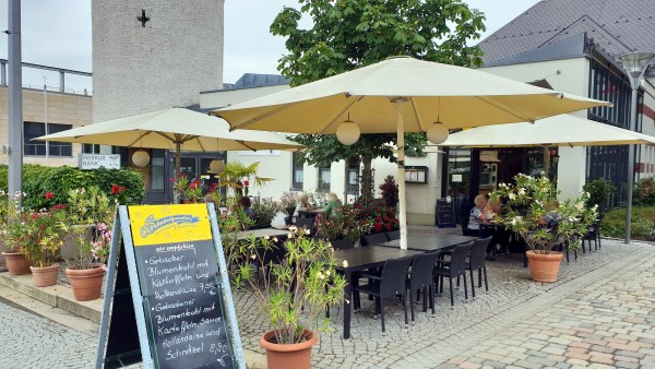 Restaurant Außenbereich, vorne noch leere Plätze. Davor Angebotstafel 