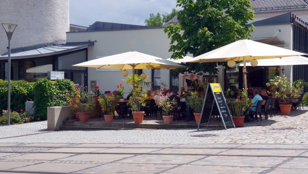 Leute sitzen unter Sonnenschirme hinter Blumentöpfe