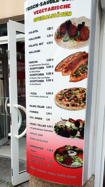 Angebotstafel mit Preisen und Bildern vom Essen, neben weißer Eingangstür