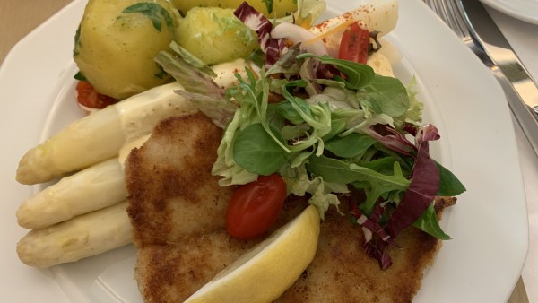 Schnitzel, Spargel und Kartoffeln auf weißem Teller. Oben drauf Rukola-Salat mit Tomate und daneben ein Stück Zitrone.