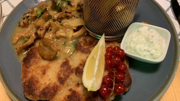 Paniertes Fleisch mit gebratenen Waldpilzen und Kartoffelröstis in Metallgitter. Dazu Zitrone, Johanissbeeren und Dip