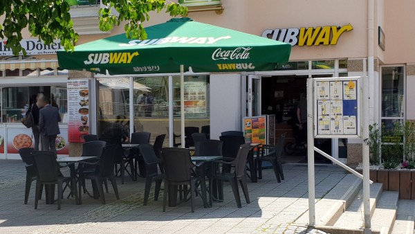 Sitzgruppen unter Sonnenschirm vor Subway-Restaurant