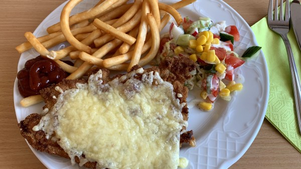 Schnitzel mit Käse und langen Pommes mit Ketchup und Salatbeilage auf Teller
