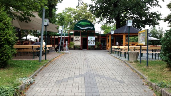 Gepflasterter Weg mit Pfeil der den Weg hinein zeigt. Rechts und links stehen Bierzeltgarnituren und gehören zum Biergarten.