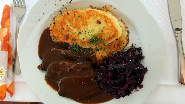 Sauerbraten mit Rotkohl und Bambes auf Teller zwischen Besteck