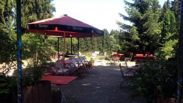 Gepflasterter Biergarten-Bereich mit Stühlen und Tischen im Wald, großteils im Schatten